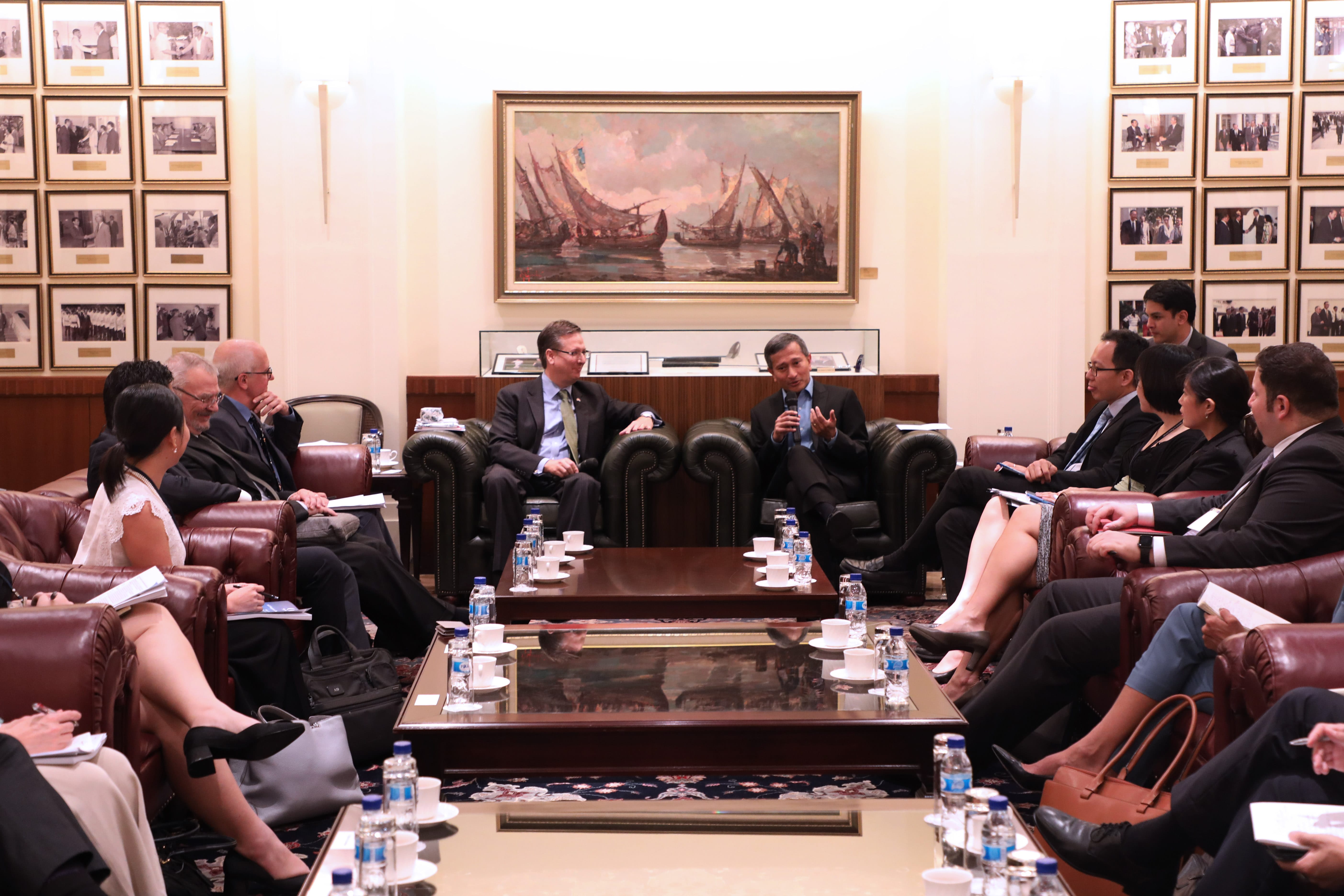People in business attire seated in leather chairs in a meeting room, painting on wall.